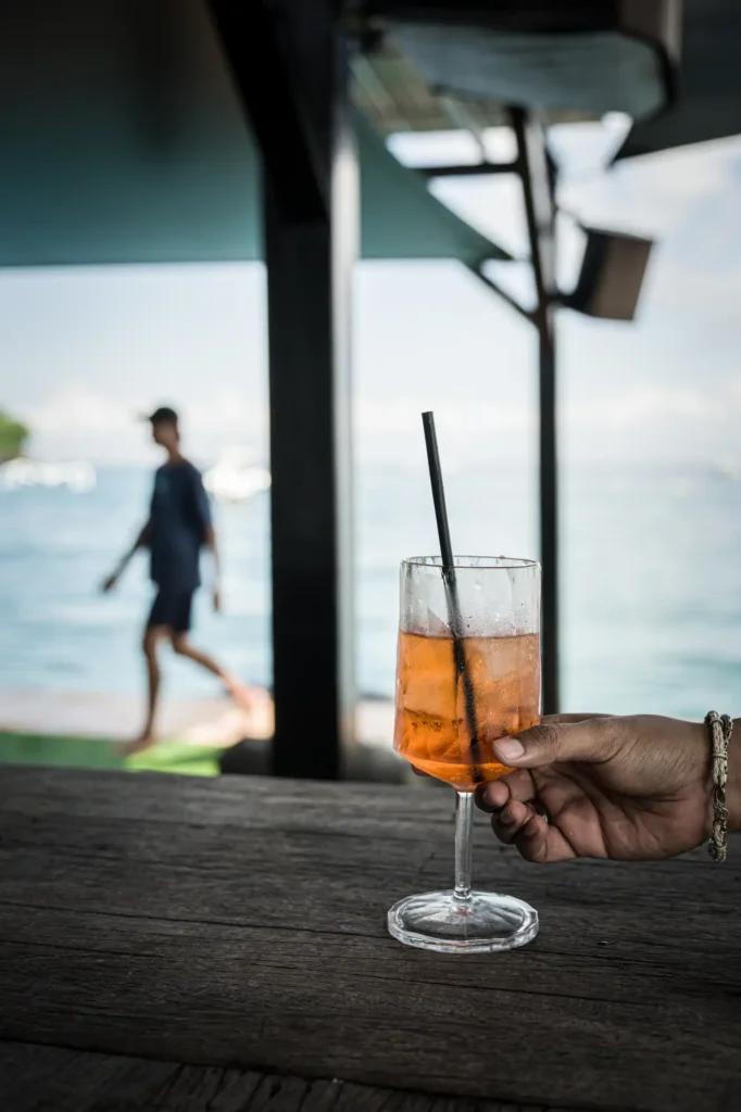 An Aperol spritz served in a stemmed glass on weathered timber decking above the rippled ocean at the Pontoon at Lago.