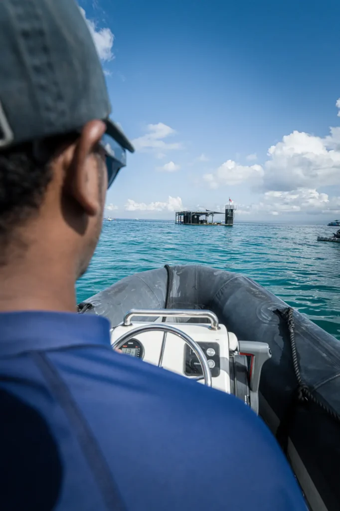 View over a Lago captain's shoulder as he pilots a tender boat across turquoise water toward the Pontoon at Lago floating bar.